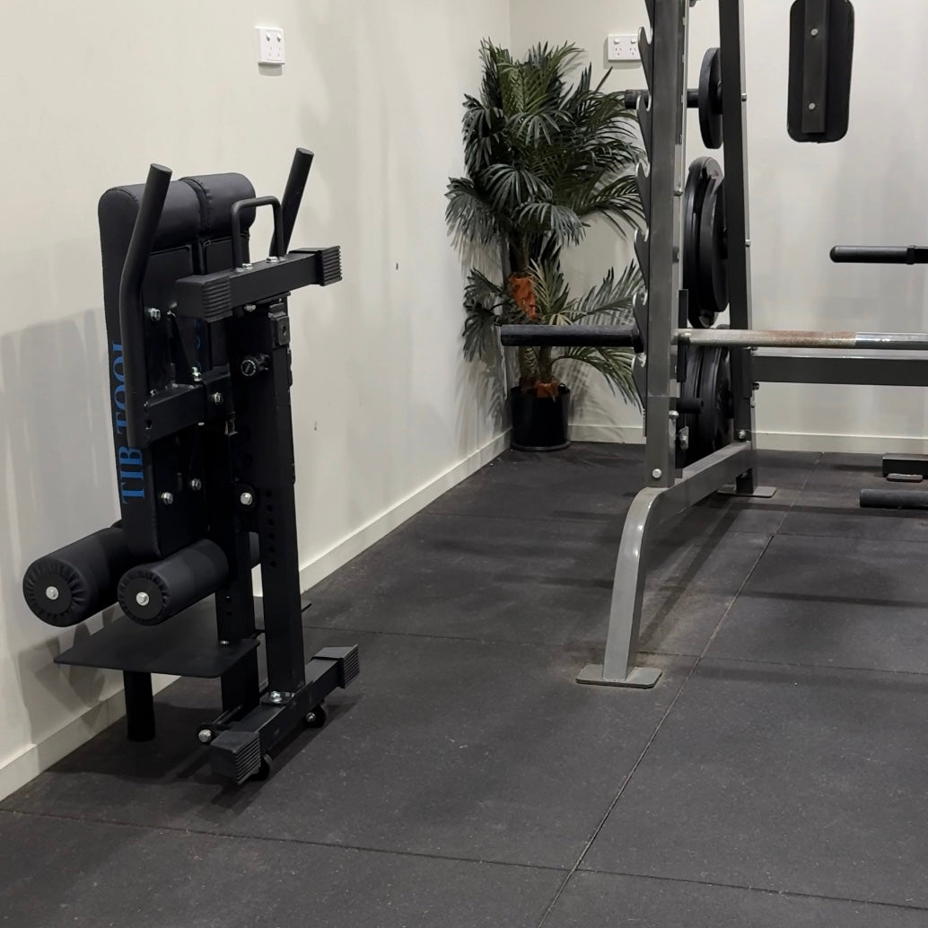 Gym equipment including a leg press machine and weight rack on a tiled floor.