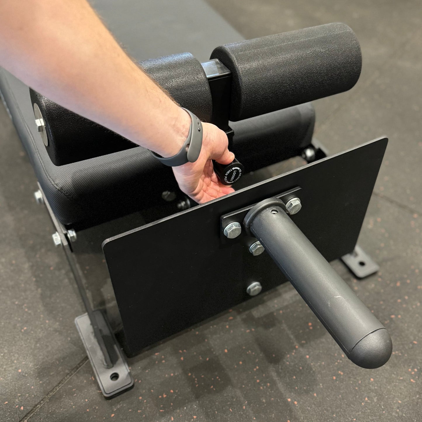 A close-up of a hand adjusting the settings on an adjustable Nordic Bar fitness equipment in a gym setting.