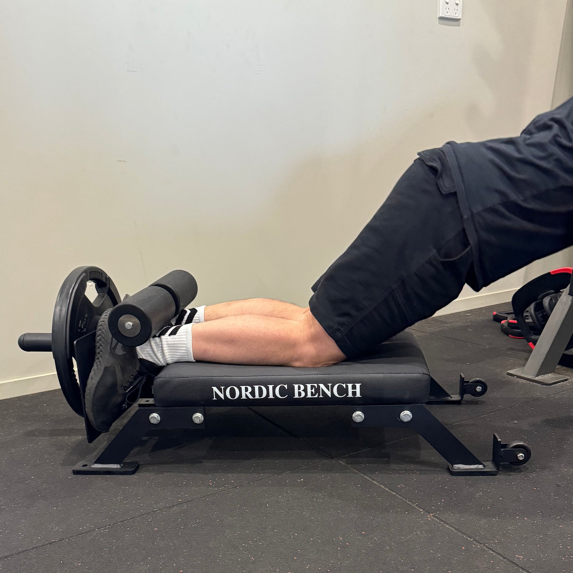 A person performing an exercise on a Nordic Bar bench, focusing on leg movements, showcasing proper form and equipment.