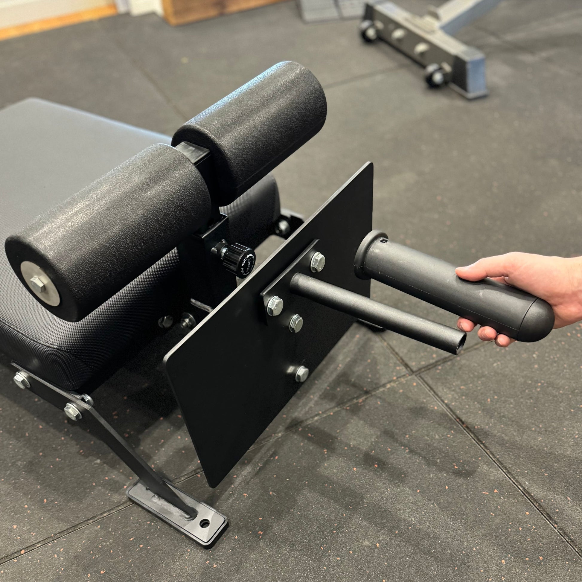 Close-up of Nordic Bar gym equipment with padded rollers and handles for exercise, situated on a gym floor.