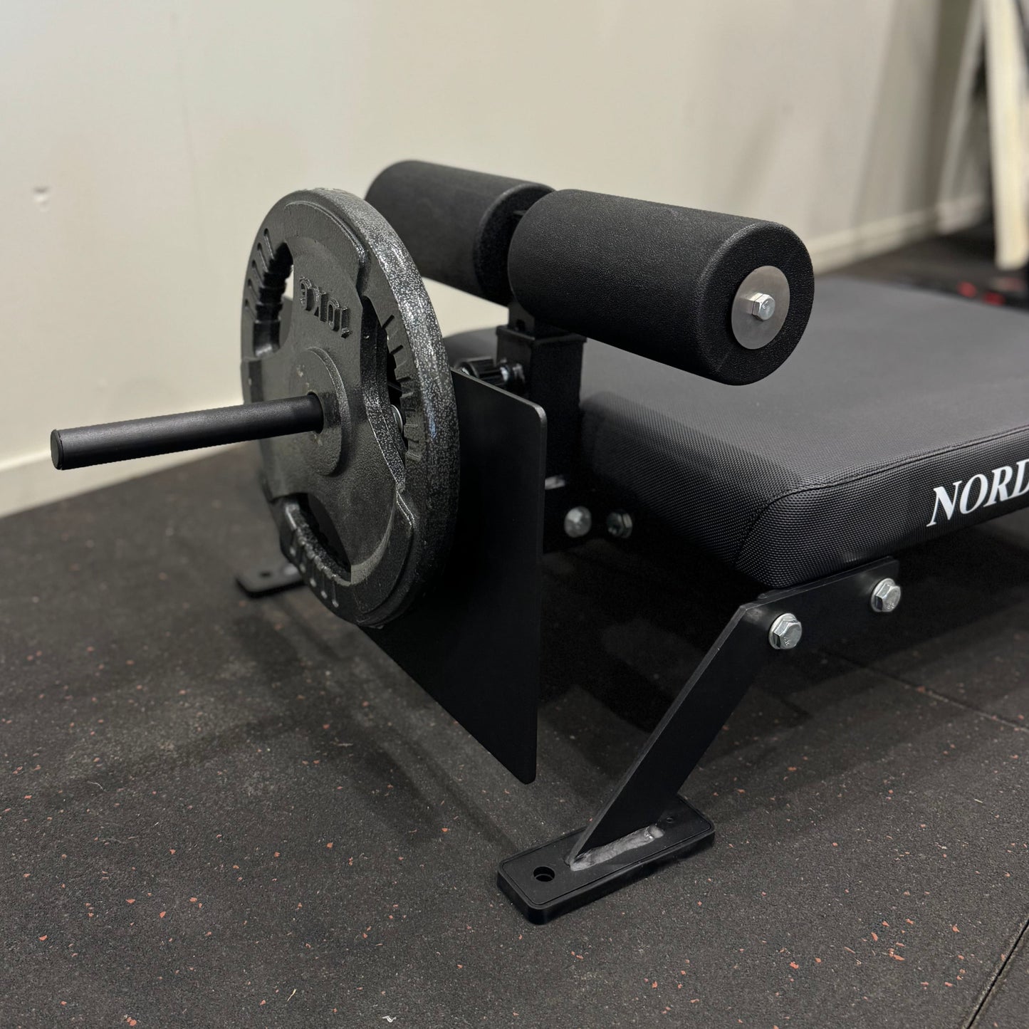 Close-up of a Nordic Bar weightlifting bench showing weights and padded leg support, ideal for strength training.