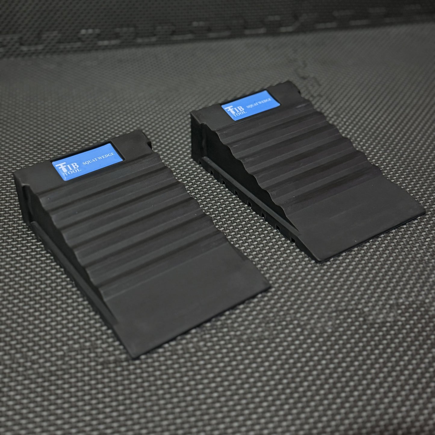 Two black squat wedges designed for improving squat form, placed on a textured surface for gym use.