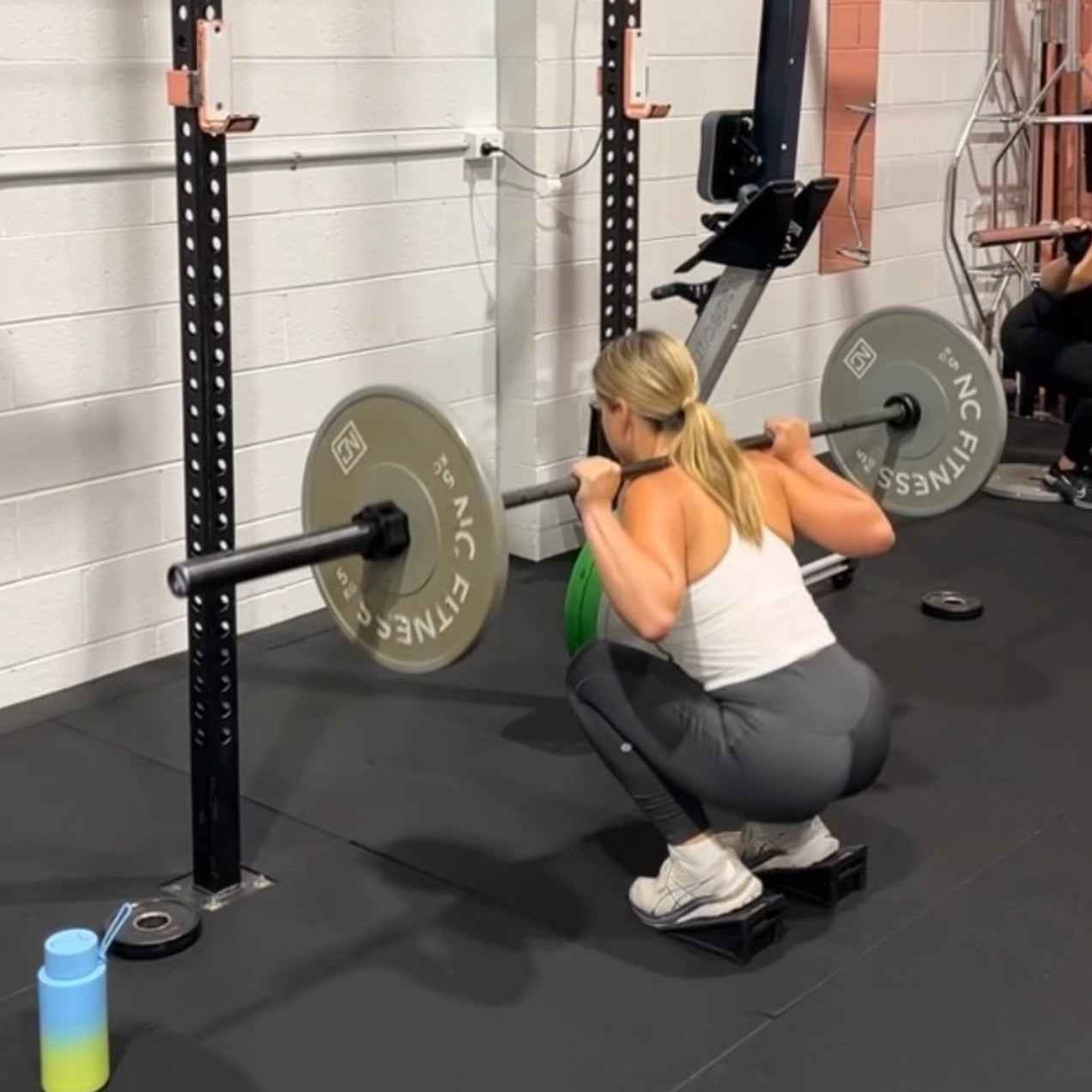 A woman performing a barbell squat using squat wedges in a gym setting, focusing on proper form and technique.