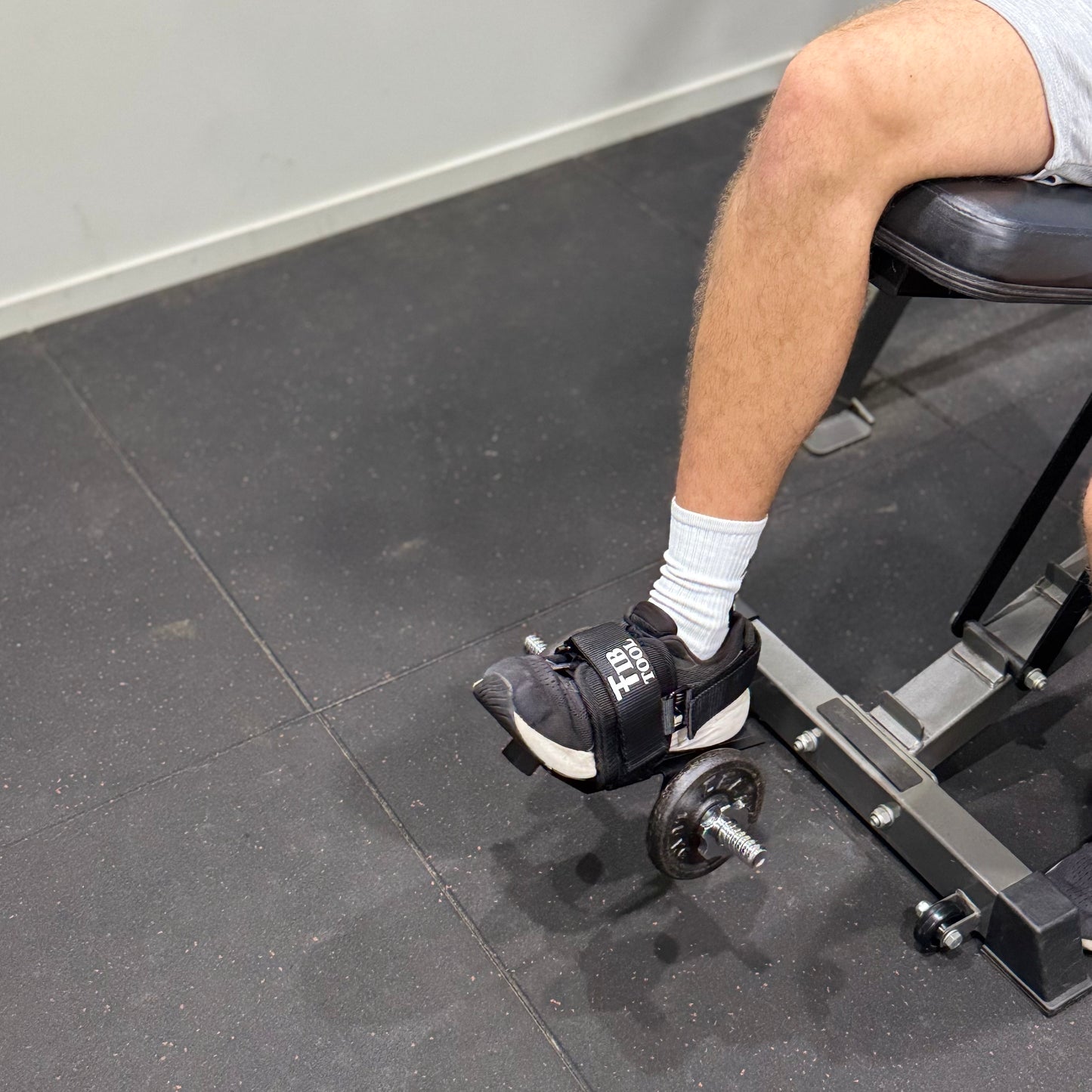 Person using a single leg isolation ankle weight for leg extensions in a gym setting.