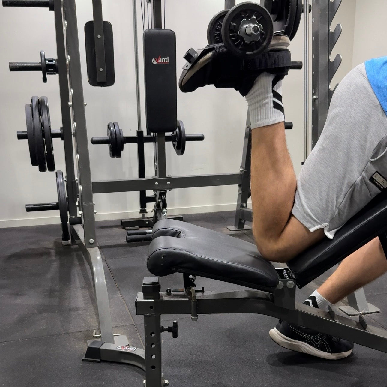 Person using a single leg isolation tib bar for hamstring curls in a gym setting.