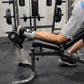 Person using a single leg tib bar for hamstring curls in a gym setting.