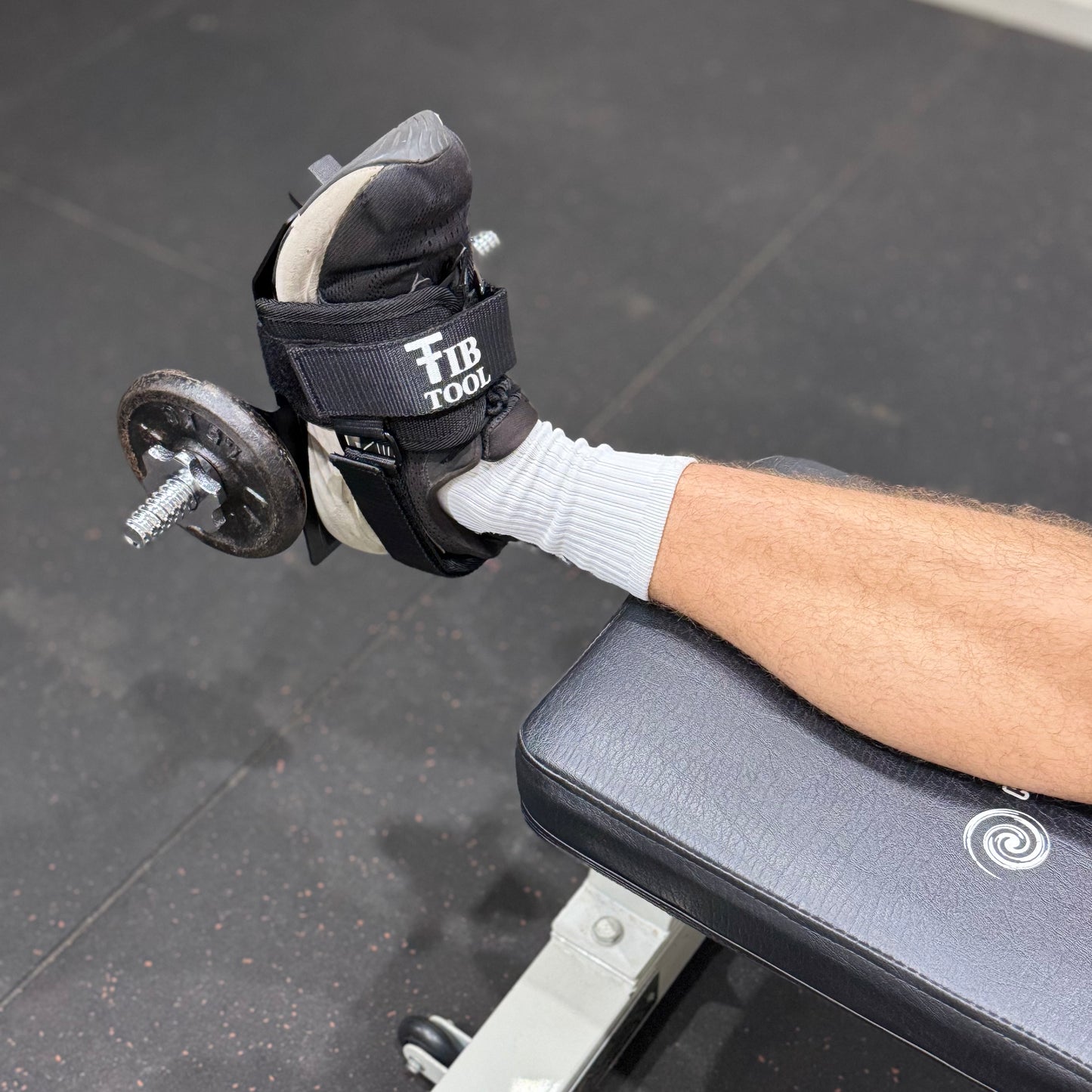Person doing tib raises with a tib bar on a weight bench in a gym setting.