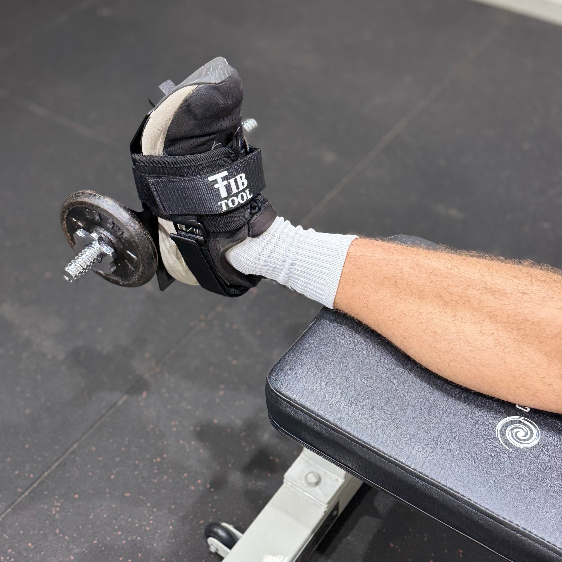 Person doing tib raises with a tib bar on a weight bench in a gym setting.